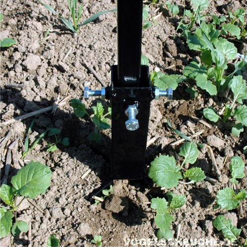 Der in den Boden eingeschlagene Bodenanker mit Halterung, umgeben von jungen Pflanzen auf dem Feld.