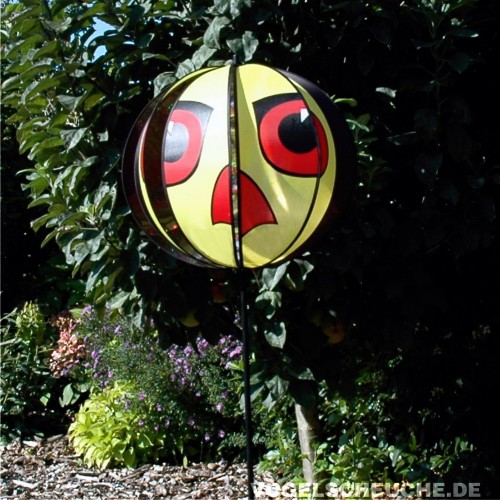 Windrotor TURBINE in Gelb auf einer Stange im Garten vor Hecke und blühenden Beeten.